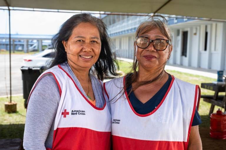 Two women stand in Red Cross vests