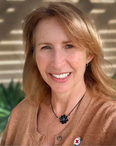 woman in brown sweater with red cross pin
