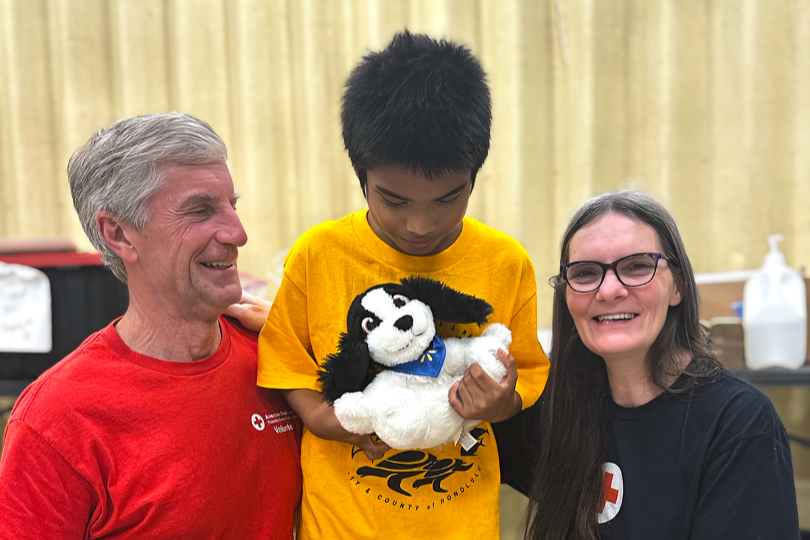 Two Red Cross volunteers pose next to young boy holding stuffed animal