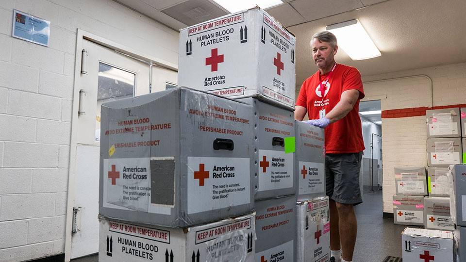 red cross volunteer pushing a cart of red cross blood boxes.