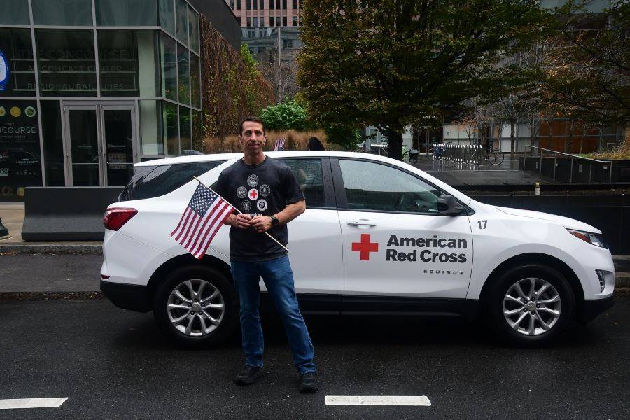 Shawn Curnew holding an American flag standing in front of a red cross car