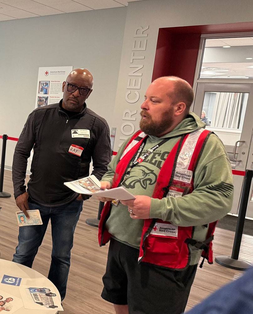 Jesse O’Brien, wearing a Red Cross vest, standing and speaking to a room full of volunteers.