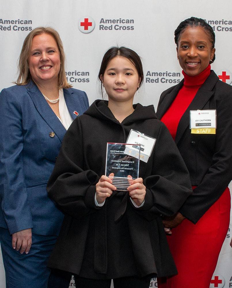 Xinyao Lin holding a Red Cross award with two Red Cross staff members standing on the left and right of Xinyao Lin.