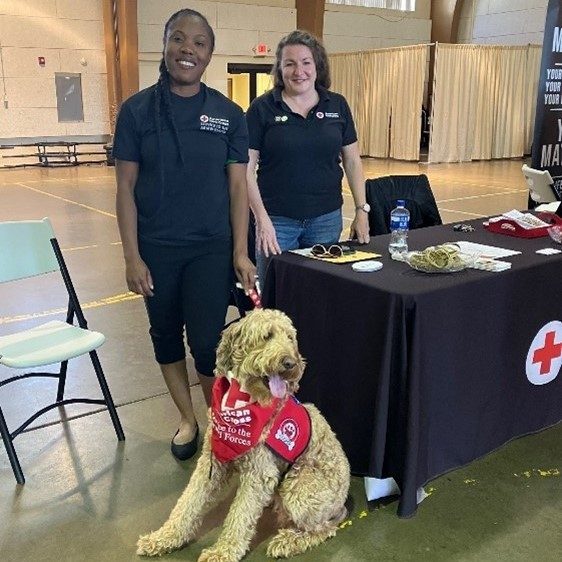 two female red cross volunteers stand behind therapy dog