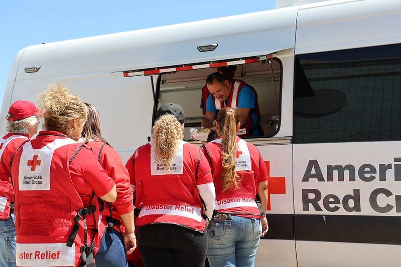 Red Cross volunteer serving food to a group of people from a food truck.
