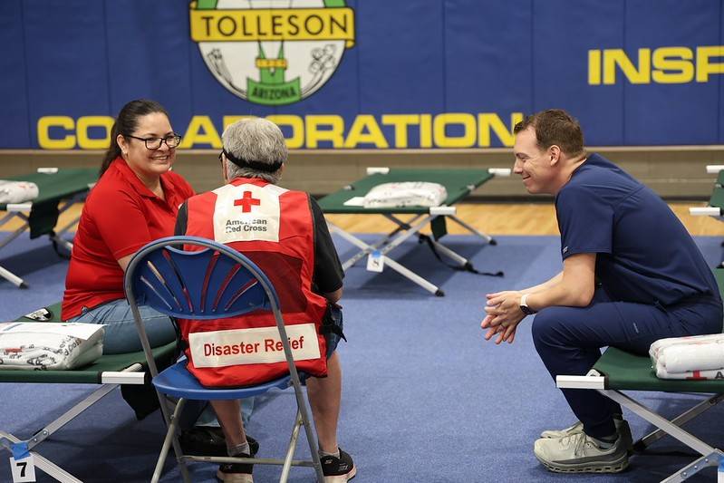 A Red Cross volunteer talking to two clients in a shelther sitting on a cot.