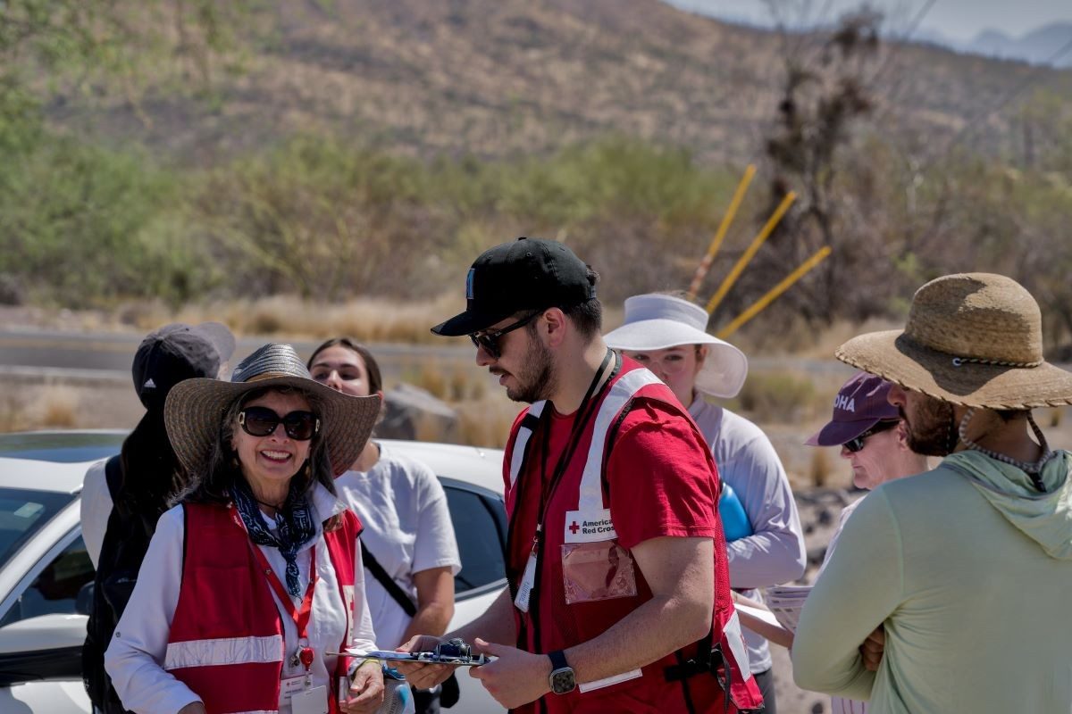 Two Red Cross volunteers in red cross vest talking to a group.