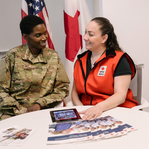 A Red Cross volunteer speaking with a service member in uniform. 
