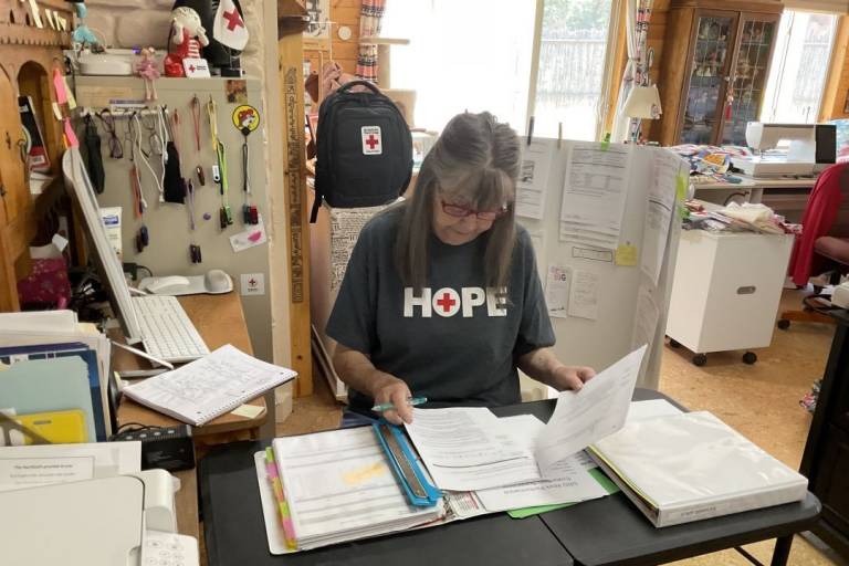 Woman in Red Cross tshirt sits at table working inside her home