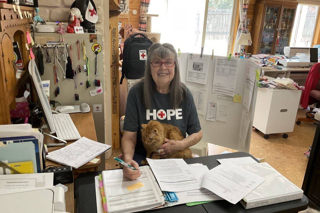 Woman in Red Cross tshirt sits at table inside her home working on paperwork
