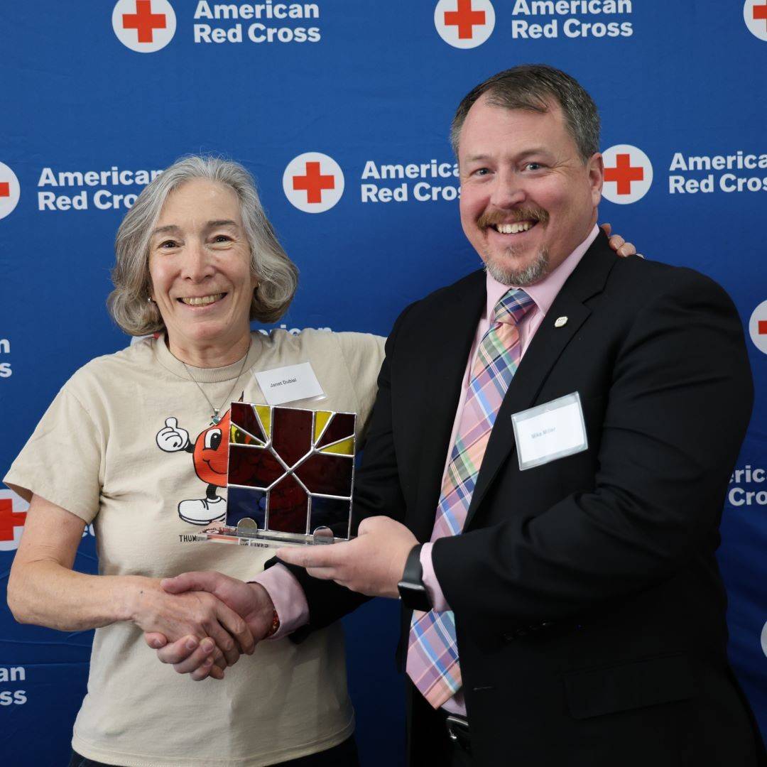 Janet shakes hand with man while holding Red Cross award