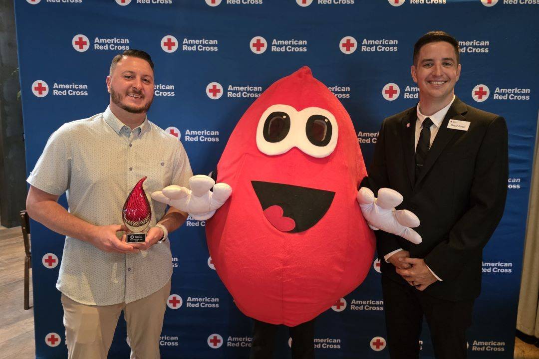 two men stand on either side of buddy the blood drop
