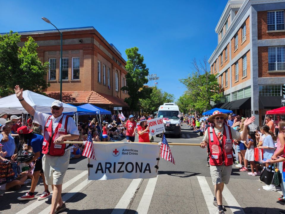 Two red cross volunteers in a parade holding red cross arizona sign