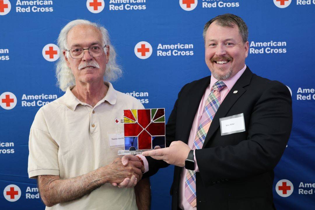 Man holds Red Cross award while shaking hands with another man