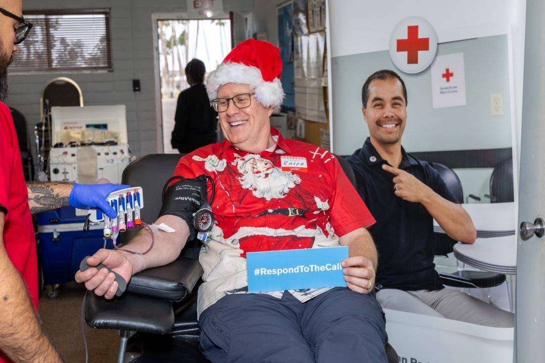 Man wearing santa hat smiles while donating blood