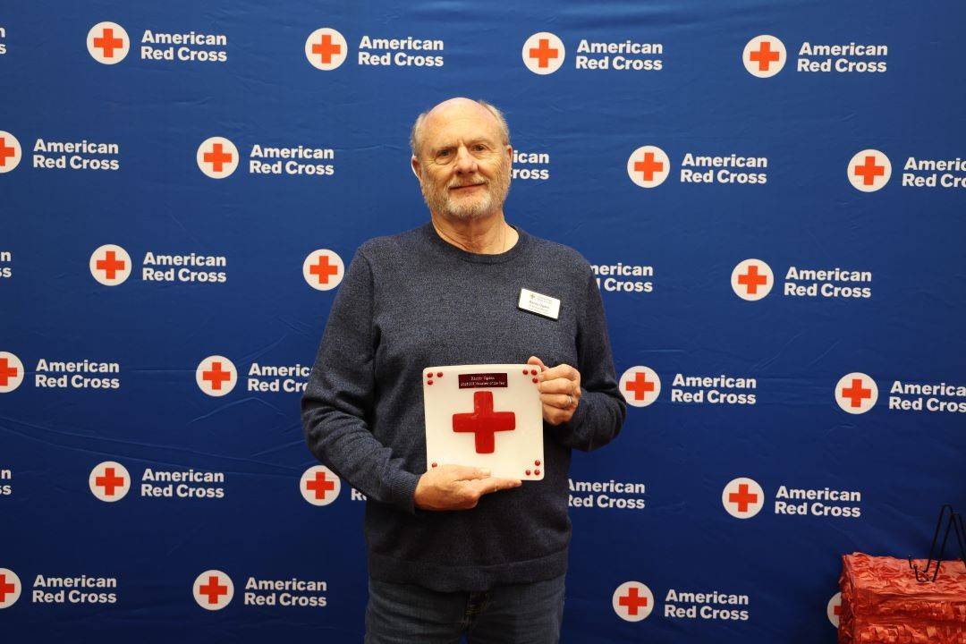 Man stands holding plaque with Red Cross logo