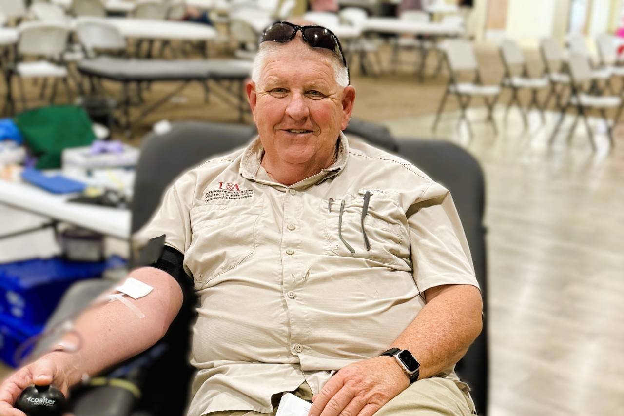 Man in tan tshirt sits in blood donation chair donating blood