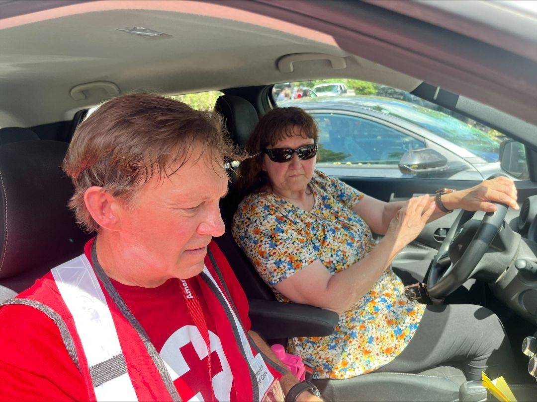 Red Cross volunteer sits in passenger seat nex to woman in driver seat of car