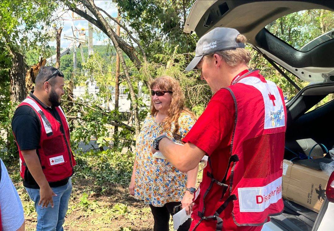 Woman stands near trunk of car talking with two Red Cross volunteers