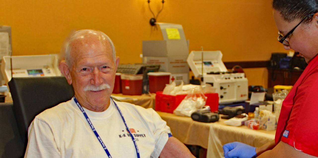 Man sits in blood donation chair while phlebotomist cleans arm