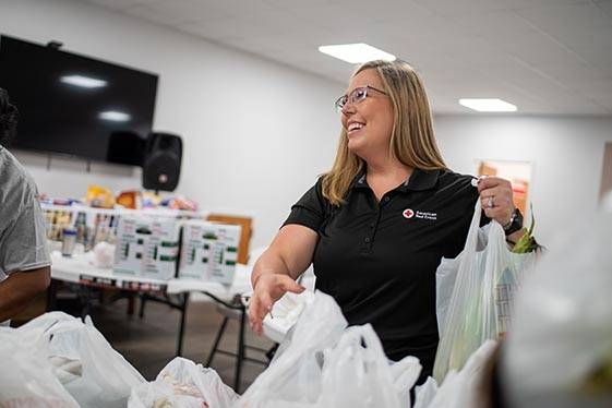 Woman in Red Cross shirt helps bag up food items
