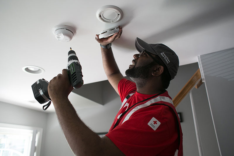 American Red Cross volunteer installing smoke alarm on a ceiling.