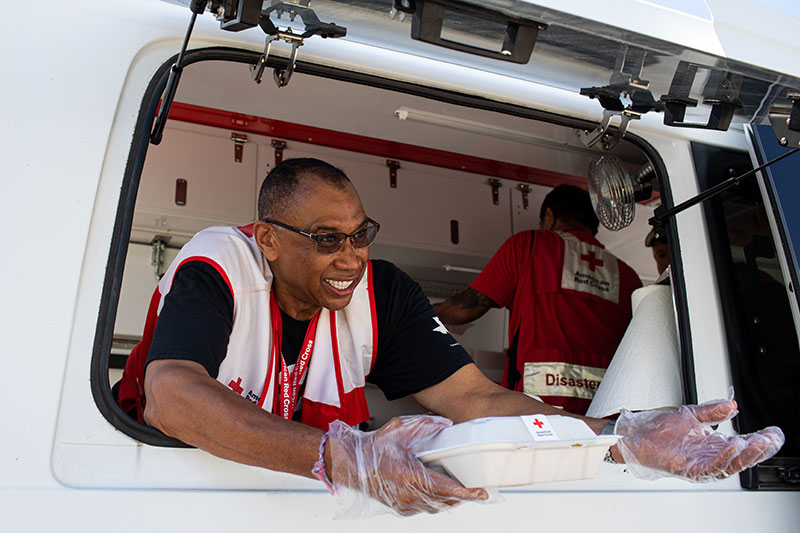 American Red Cross volunteer handing out food from a Red Cross vehicle..