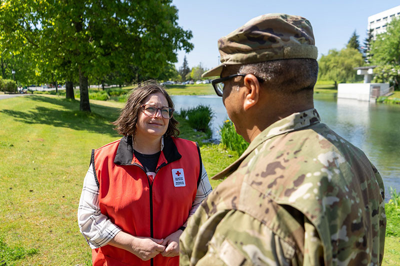 American Red Cross volunteer speaking to a military member next to a lake and trees.