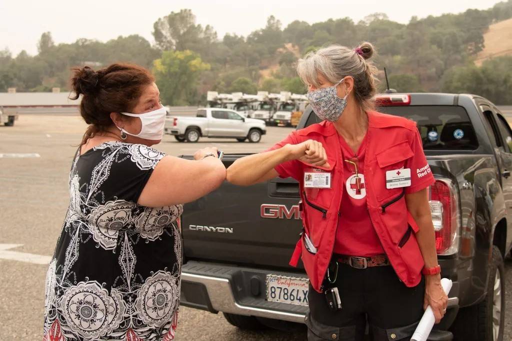 Two women wearing masks bump elbows 