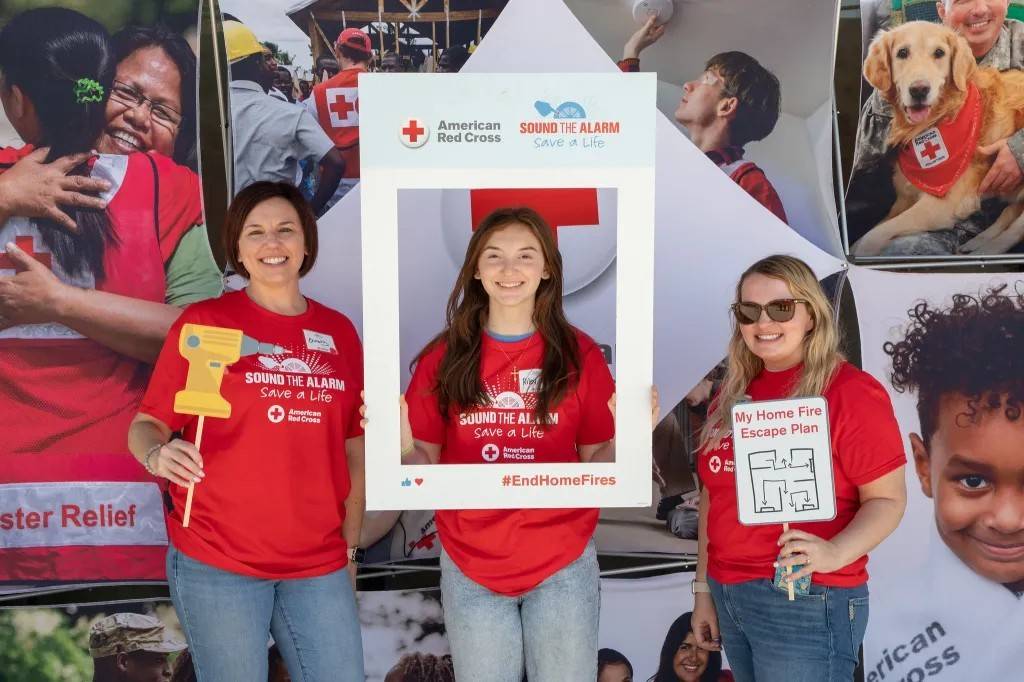 Three women stand in front of Red Cross banner with signage promoting Sound the Alarm
