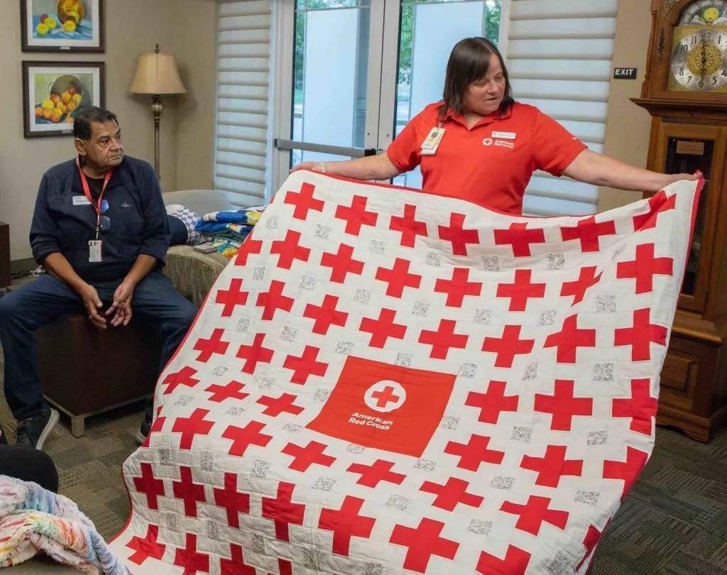 Woman holds quilt stiched with Red Cross logo