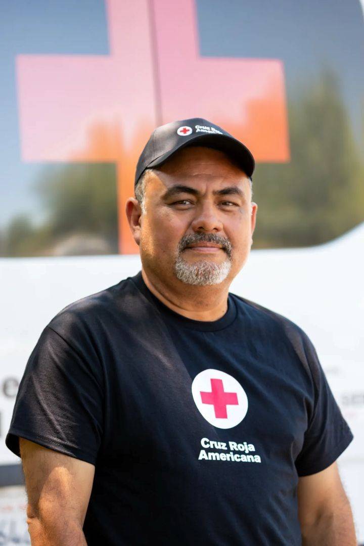 Man stands in front of Red Cross vehicle in Red Cross shirt and hat
