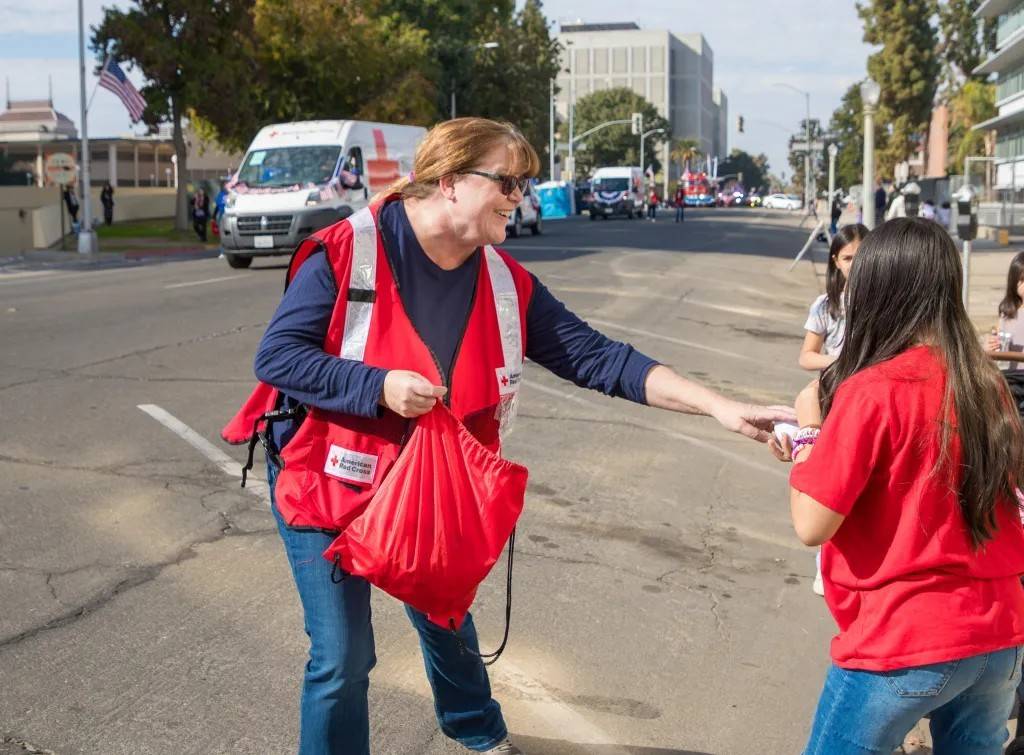 Woman in Red Cross vest hands items to youth