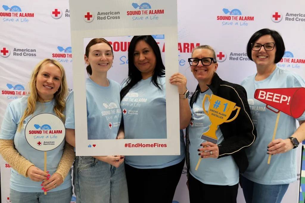 Group of women stand in front of Red Cross banner