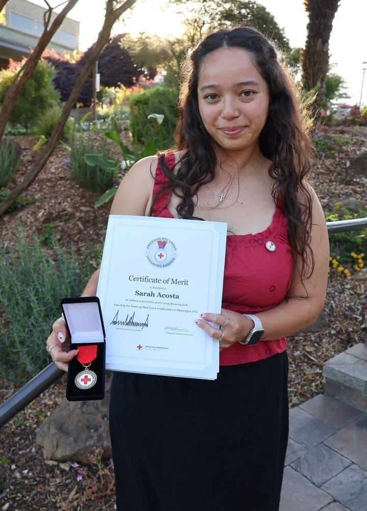Sarah stands outside holding Red Cross lifesasving award