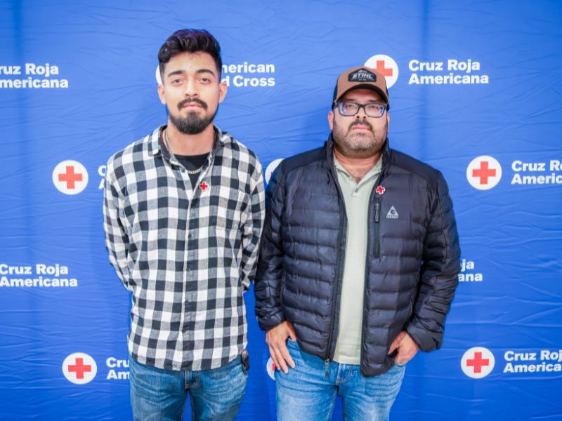 two people standing in front of red cross backdrop