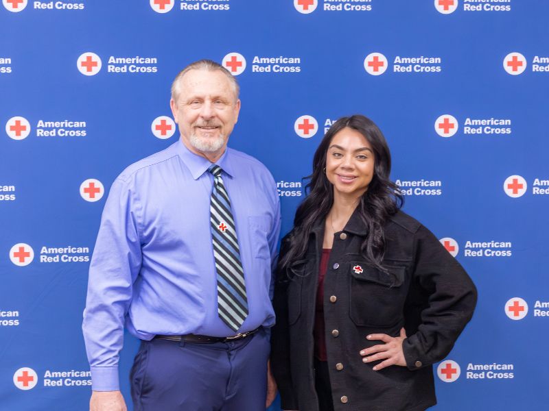 man and woman in front of red cross backdrop