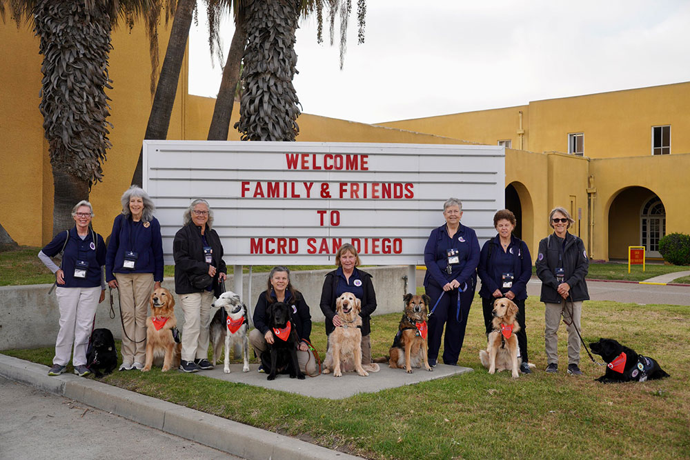 group pic of service dogs with their trainers in front of the mcrd san diego sign.