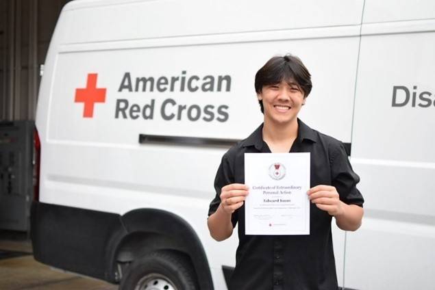Man holds paper lifesaving award in front of Red Cross van