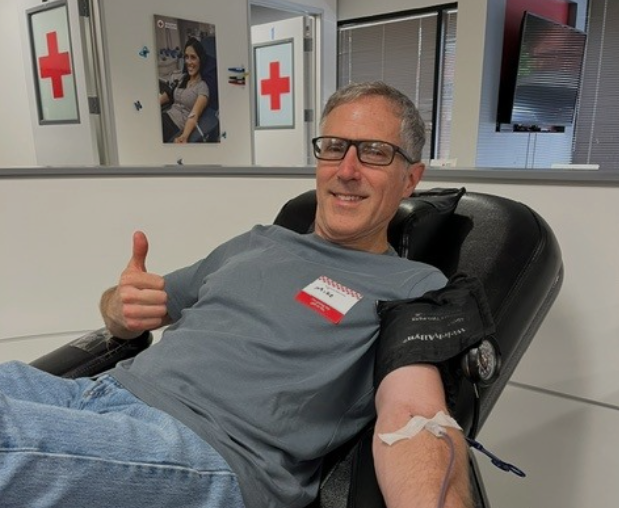 Man in gray tshirt donates blood while giving a thumbs up