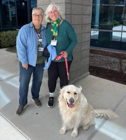 Two women stand behind dog on leash