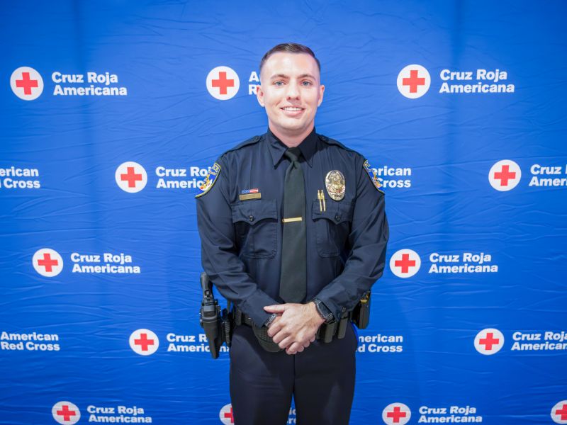 officer standing in front of red cross backdrop