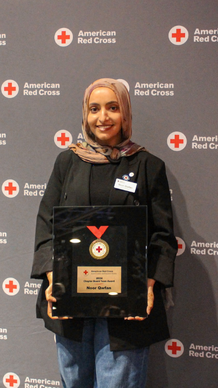Noor holding an award in front of an american red cross sign.