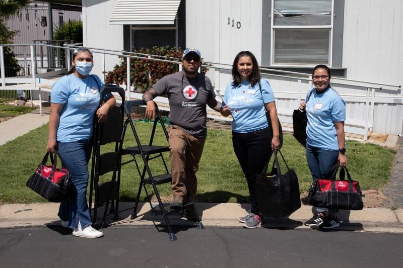 Red Cross volunteers getting ready to install smoke alarms pose in front of a house.