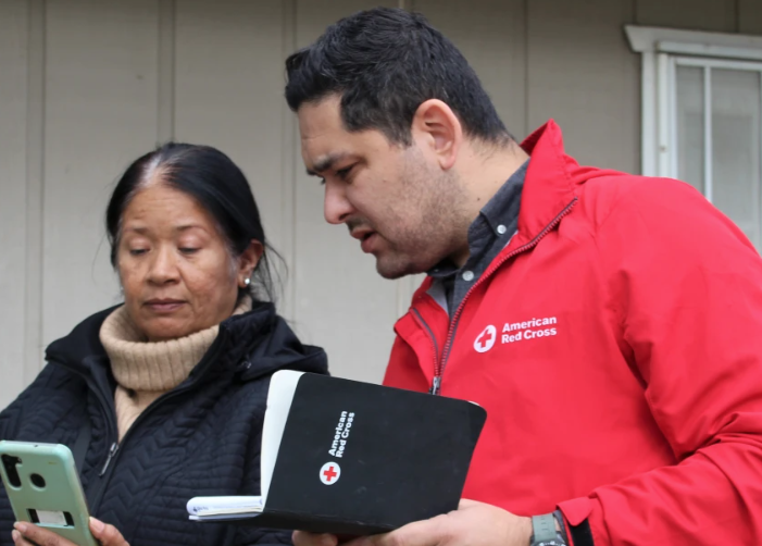 Marcos Osorio with a client holding a red cross notebook.