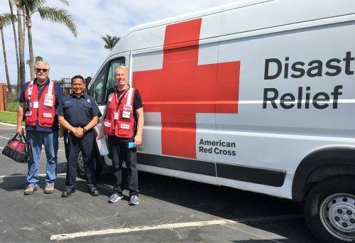 Red Cross volunteers getting ready to install smoke alarms pose in front of a house.