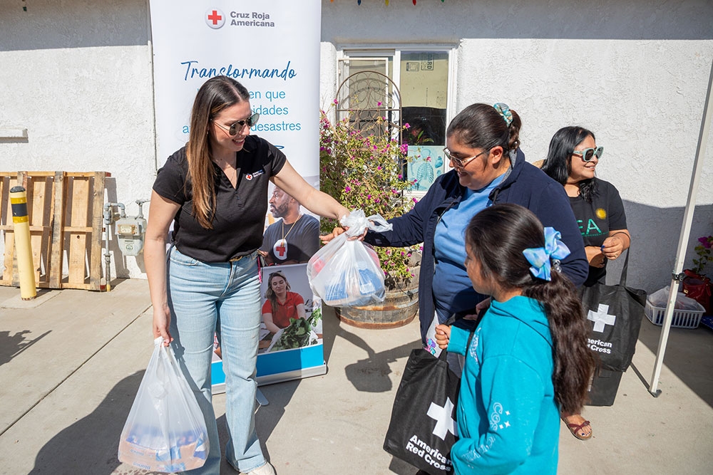 Red Cross worker hands bag of supplies to another person.