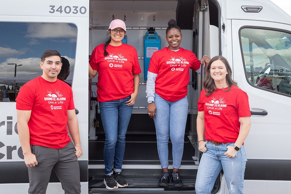 Four Red Cross sound the alarm volunteers standing next to a Red Cross van.
