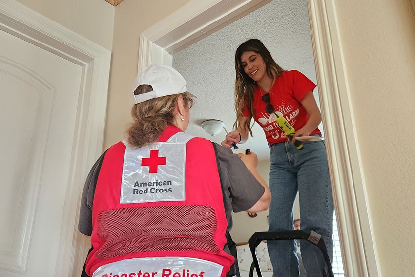Two Red Cross volunteers installing a smoke alarm in a home.