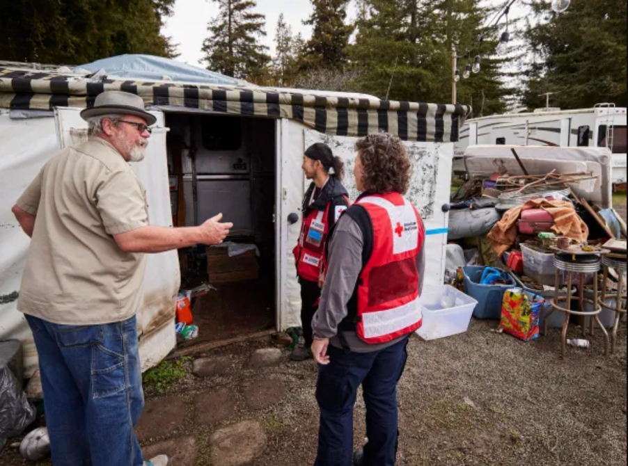 Resident at Mission Farm RV Park speaking wtih Red Cross volunteers in front of his RV draped in tarps
